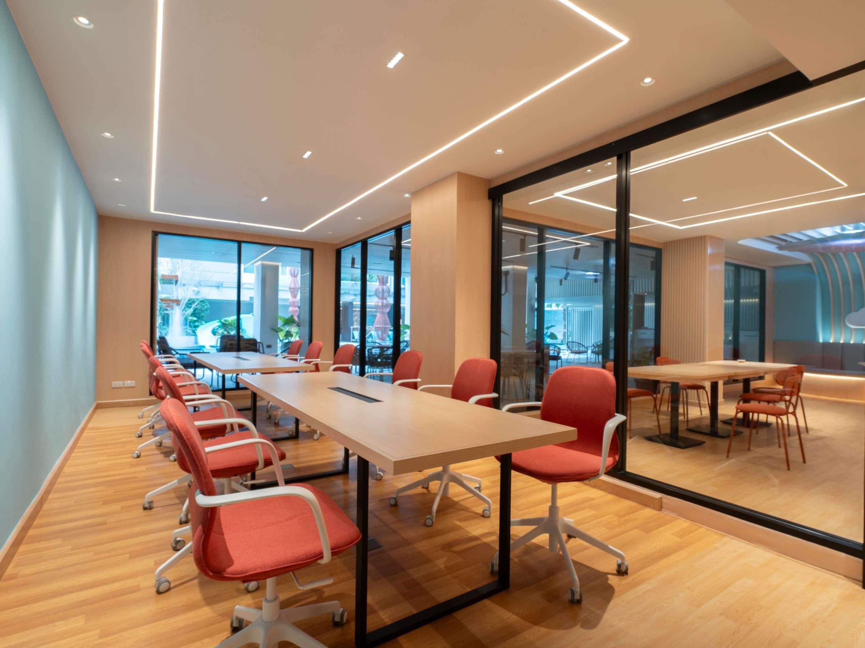 A modern conference room with a long table, red chairs, glass walls, and a view of the outside.