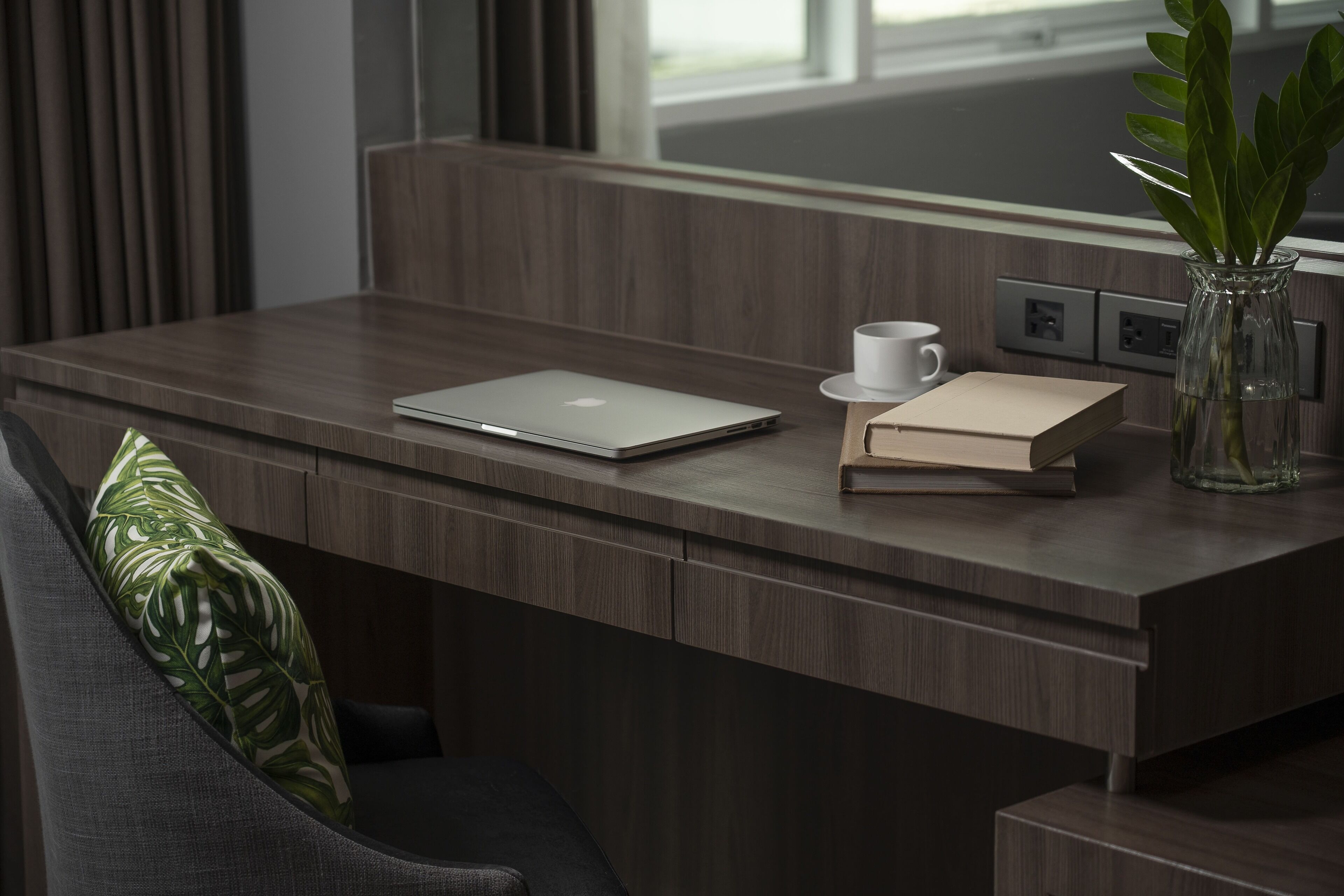 Et moderne skrivebord med en bærbar computer, en hvid kop, en bog og en vase med en plante.