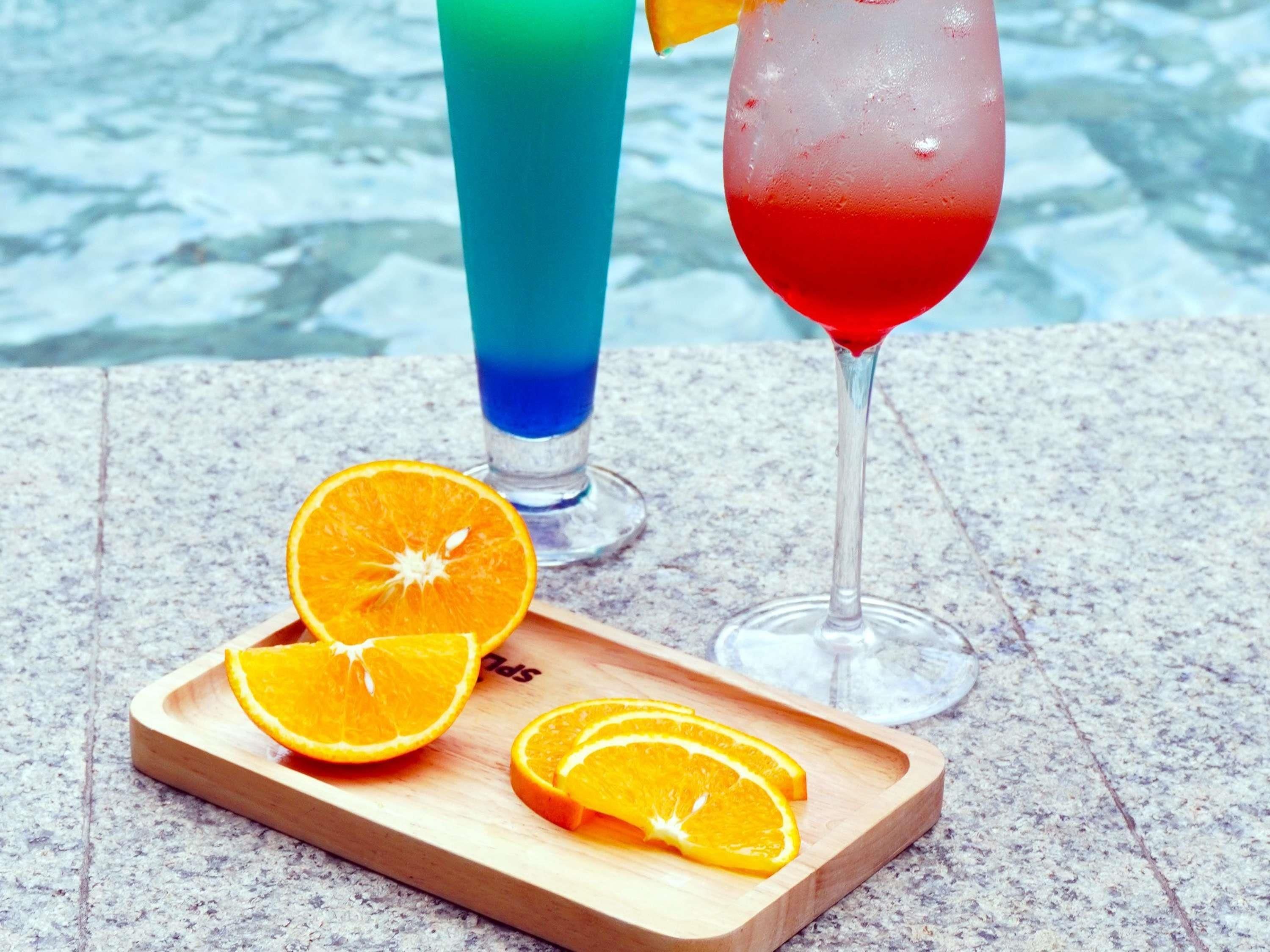 Una bandeja de madera con rodajas de naranja y dos vasos de bebidas sobre una superficie de piedra.