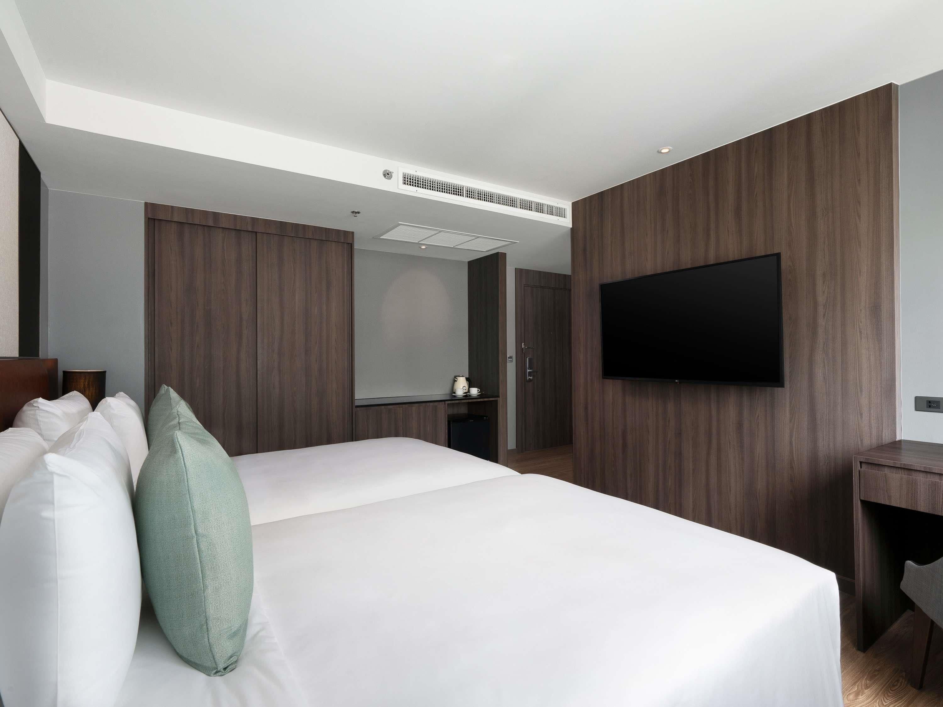 A hotel room with a large bed, a flat-screen TV mounted on the wall, and a desk with a chair.