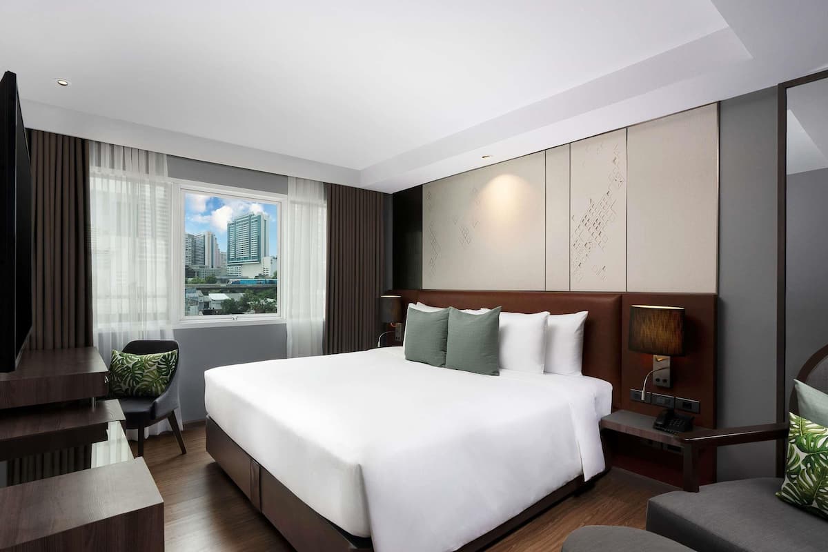 A modern hotel room with a large bed, a desk, a chair, and a view of the cityscape.