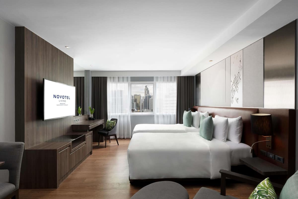 A modern hotel room with a bed, a desk, a TV, and a view of the city.