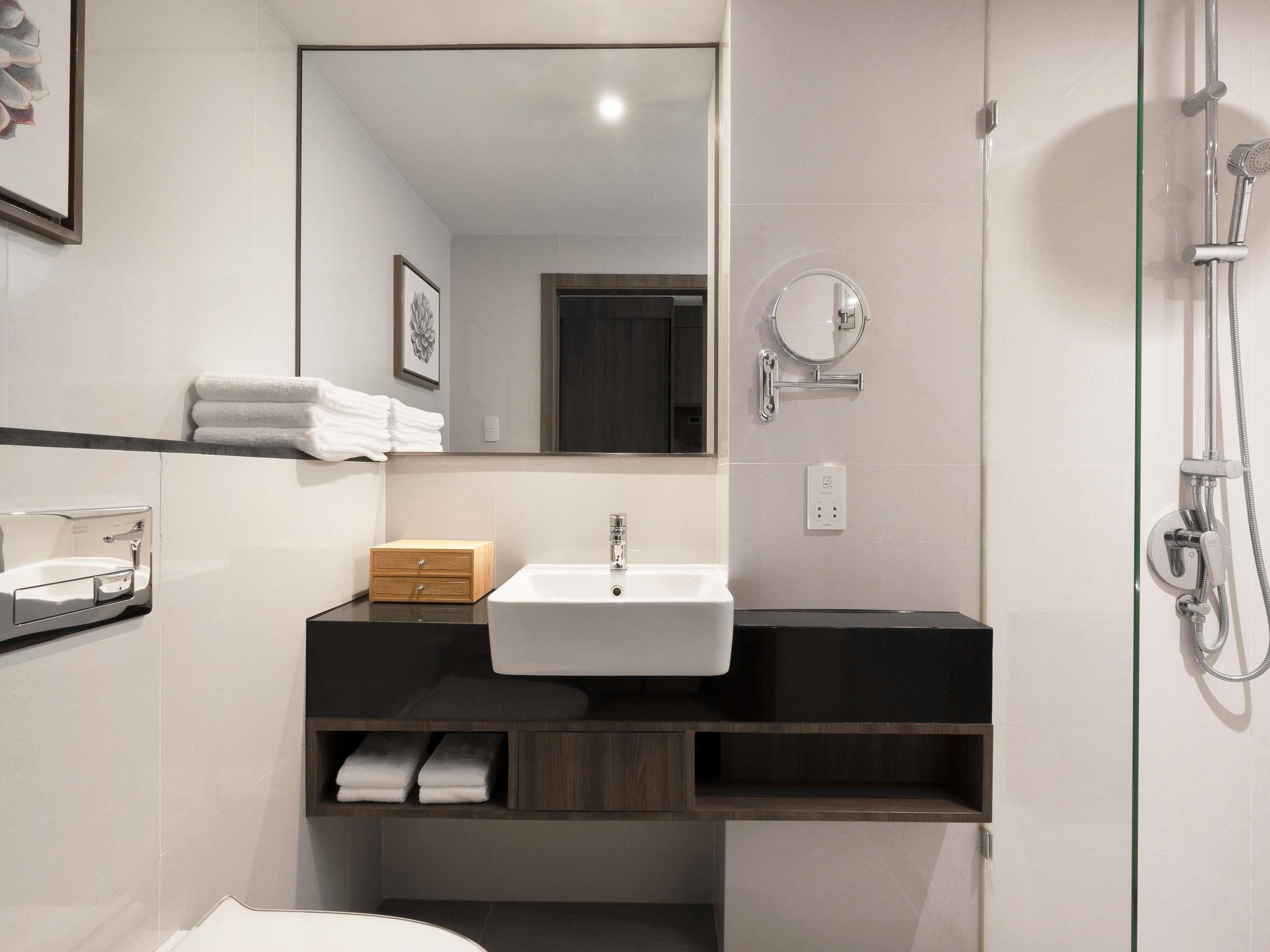 Un baño moderno con lavamanos blanco, tocador de madera, toallero, espejo y ducha.