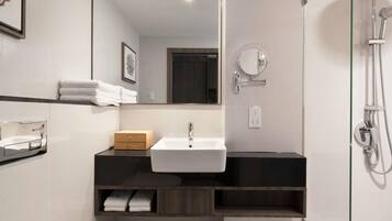 A modern bathroom with a white sink, wooden vanity, towel rack, mirror, and shower.