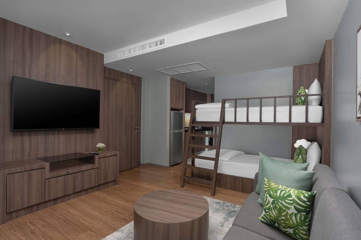 A modern living room with a TV, wooden furniture, a bunk bed, and a grey sofa.