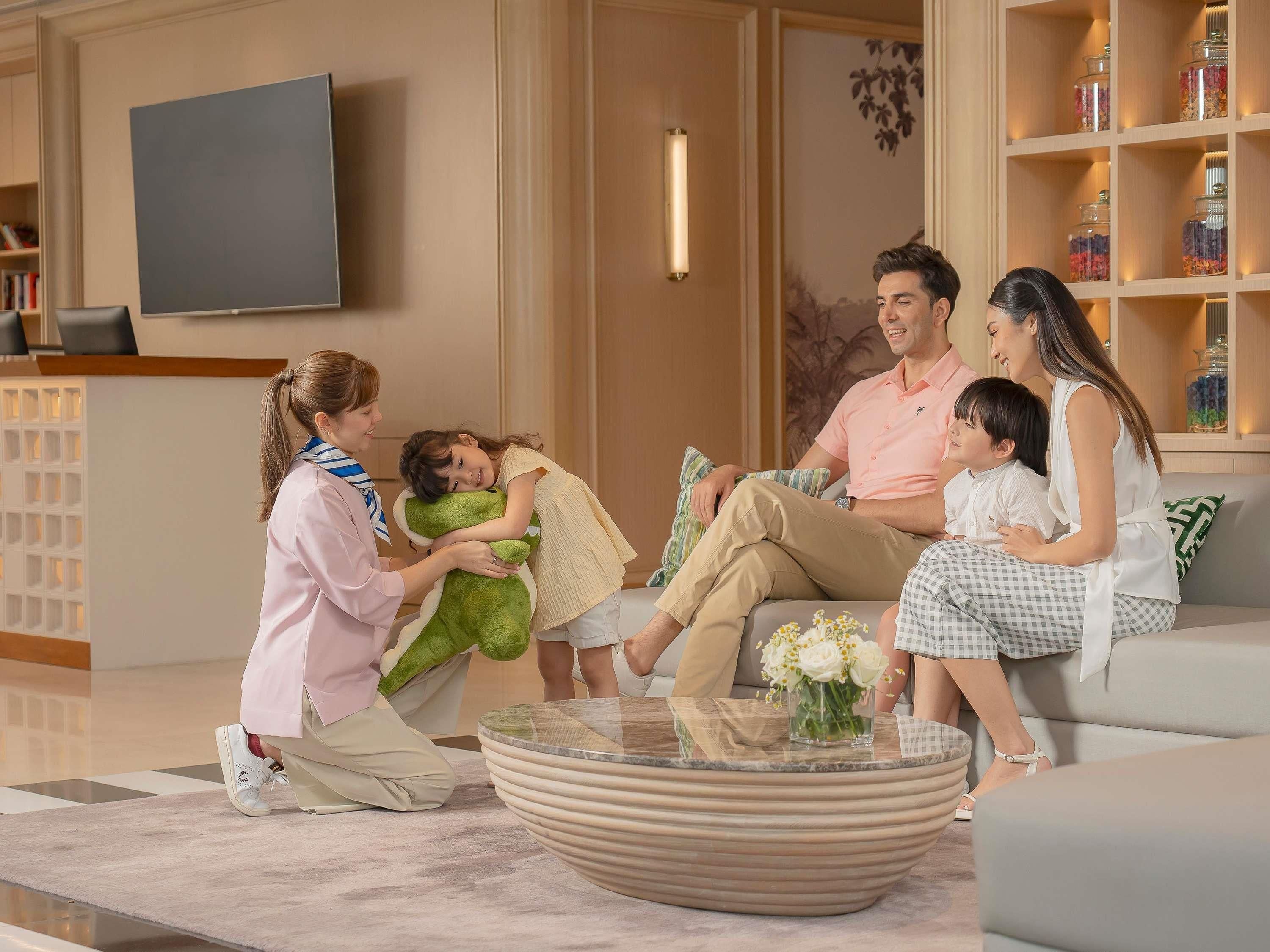 Eine Familie in einem modernen Wohnzimmer mit einem Flachbildfernseher, einem runden Couchtisch und einem Bücherregal mit dekorativen Gläsern.