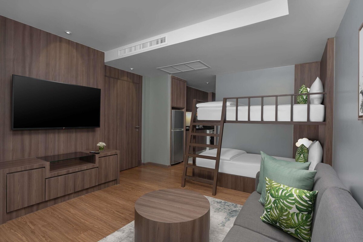 A modern living room with a TV, wooden furniture, a bunk bed, and a grey sofa.