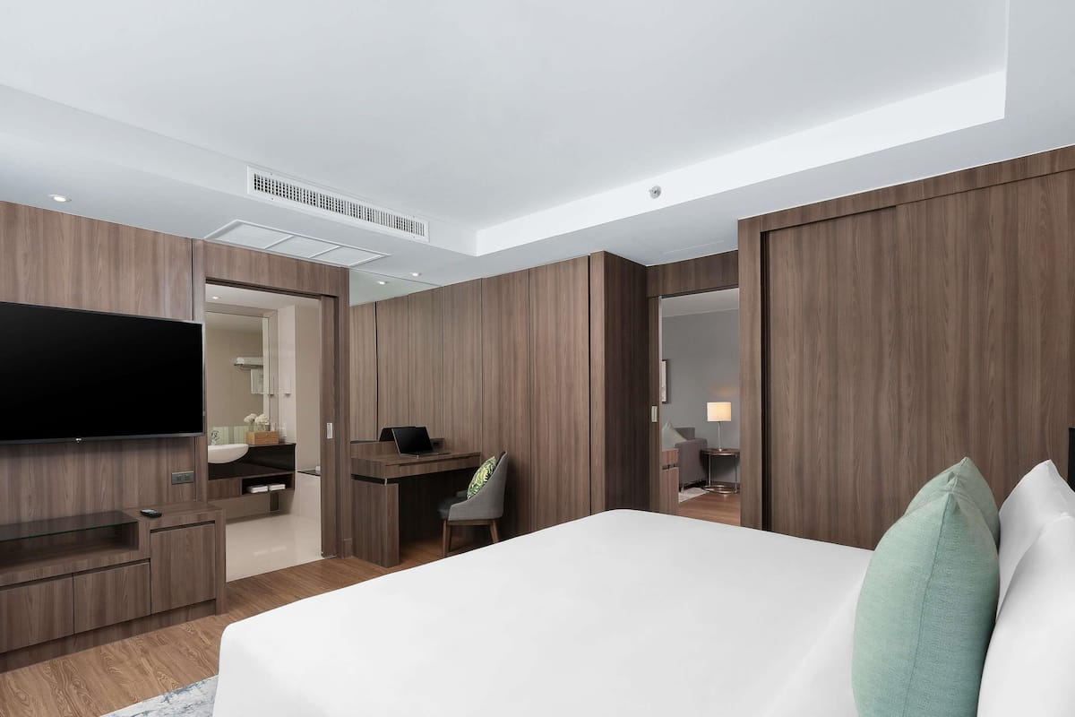 A modern hotel room with a large bed, a desk, a television, and a bathroom visible through an open door.