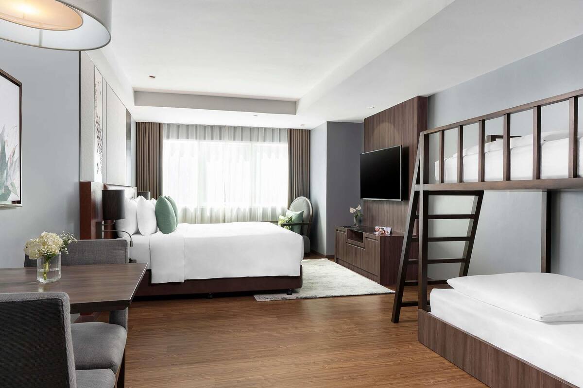 A hotel room with a bed, a desk, a TV, and a bunk bed.