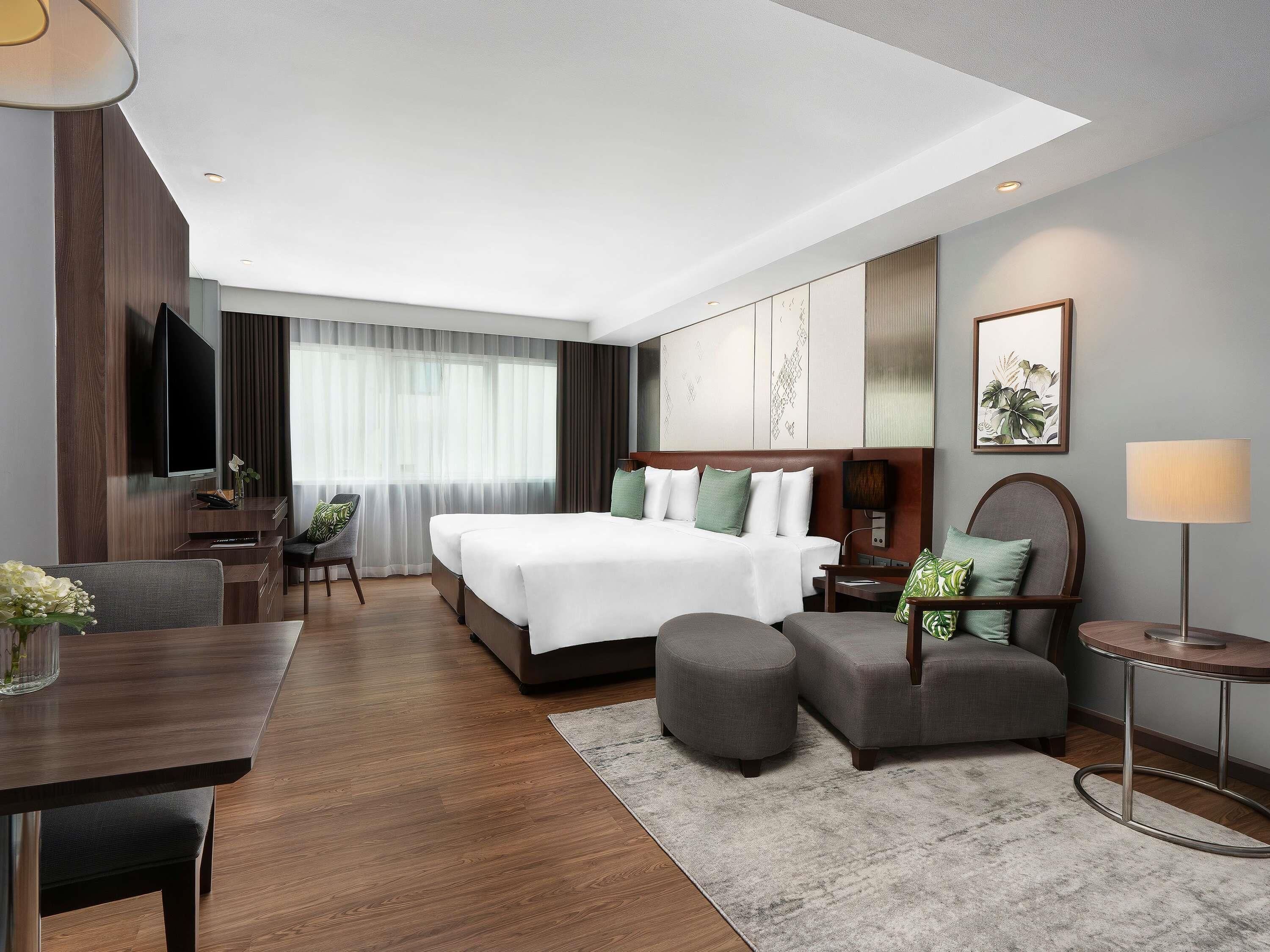 A modern hotel room with a large bed, a desk, a chair, a TV, and a window with curtains.