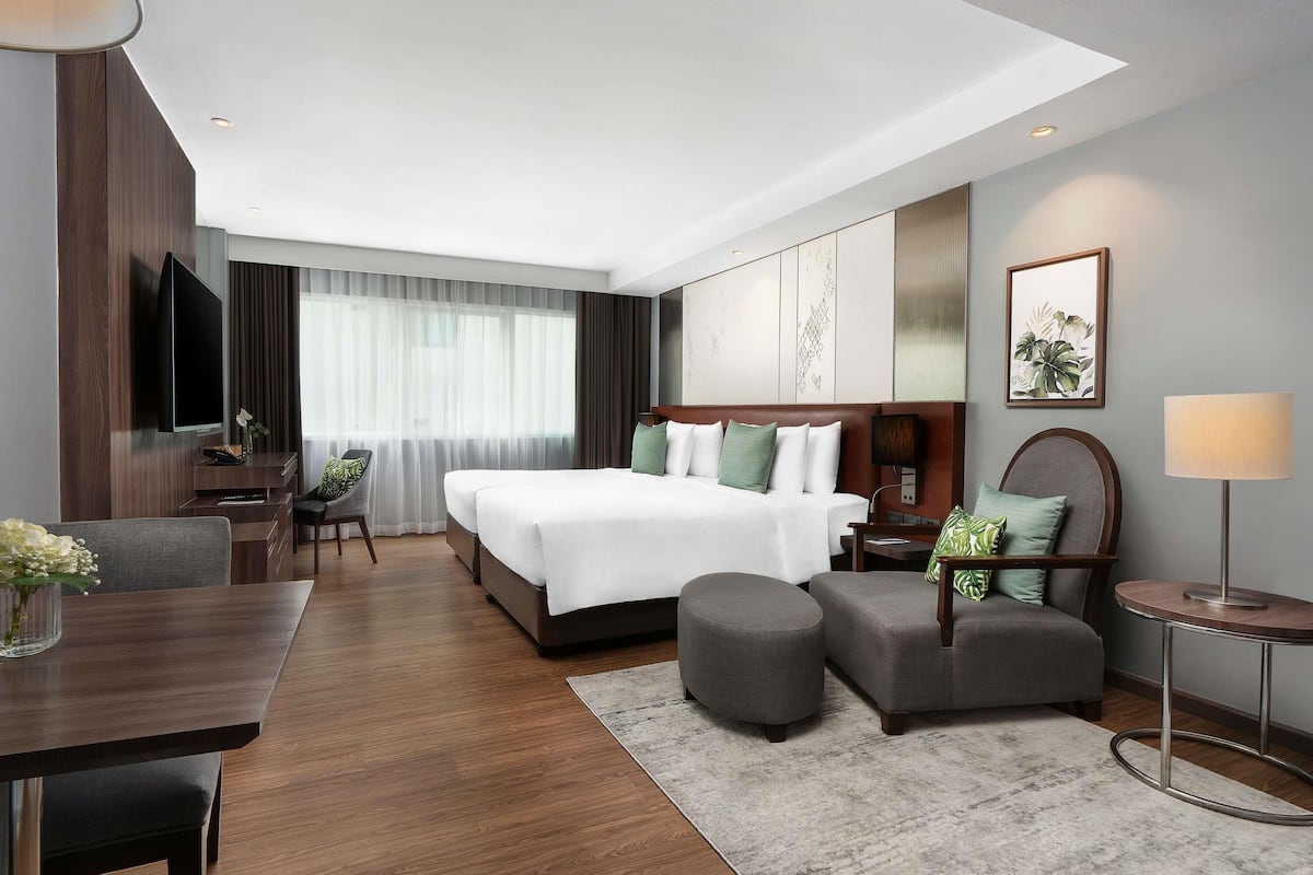 A modern hotel room with a large bed, a desk, a chair, a TV, and a window with curtains.