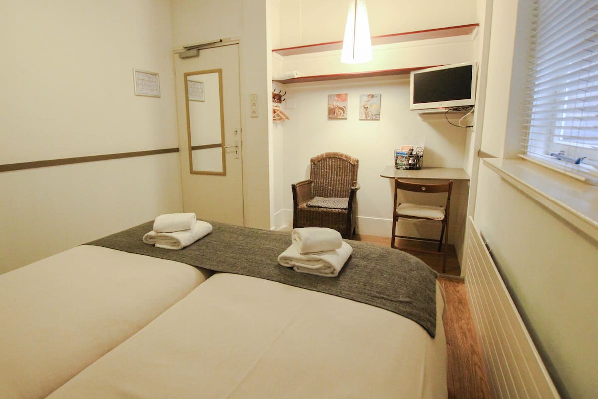 Habitación de hotel con dos camas, una silla, un escritorio, un televisor y una ventana con persianas.