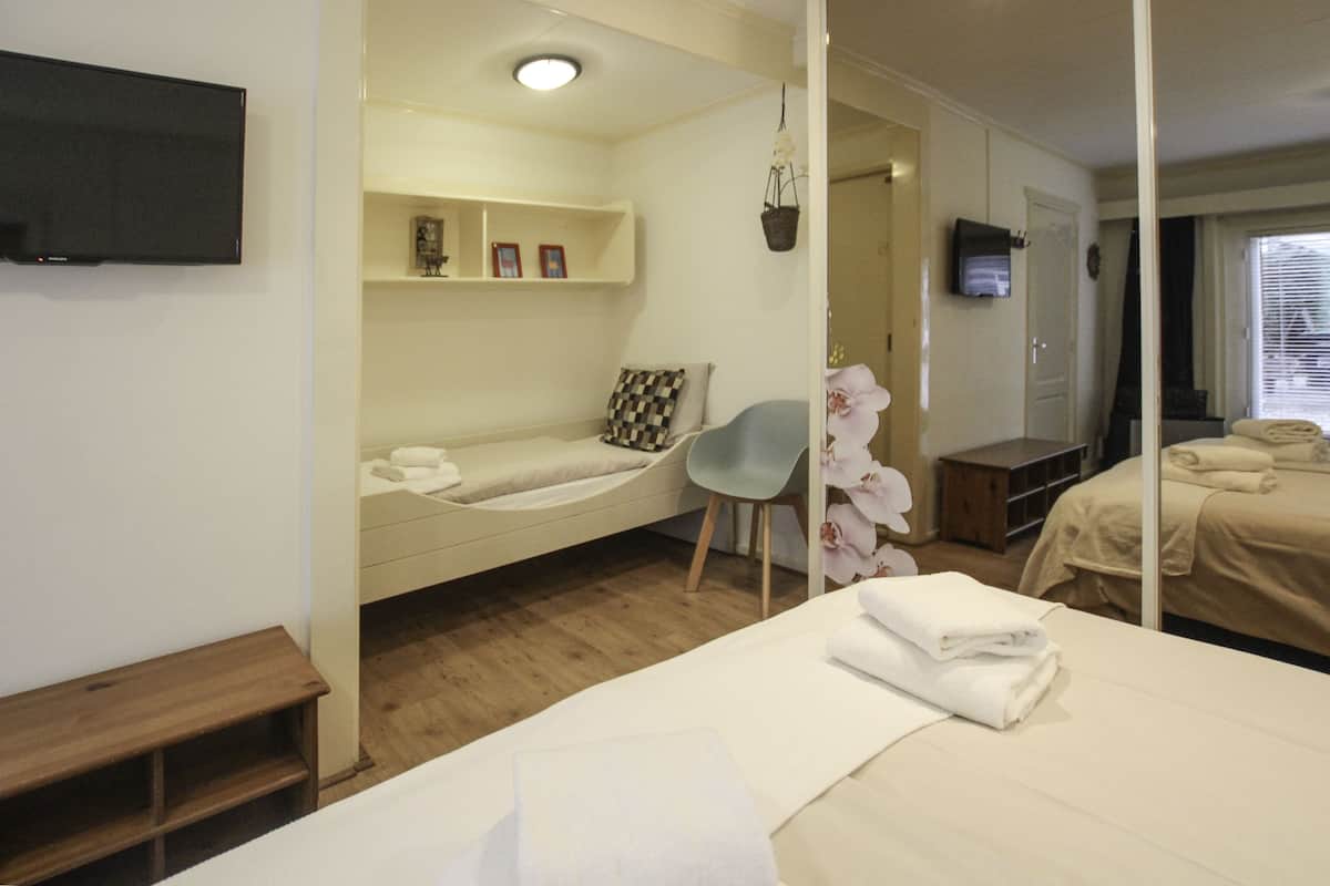 Una habitación de hotel con cama, una silla, un televisor, una mesita y un estante con fotografías.