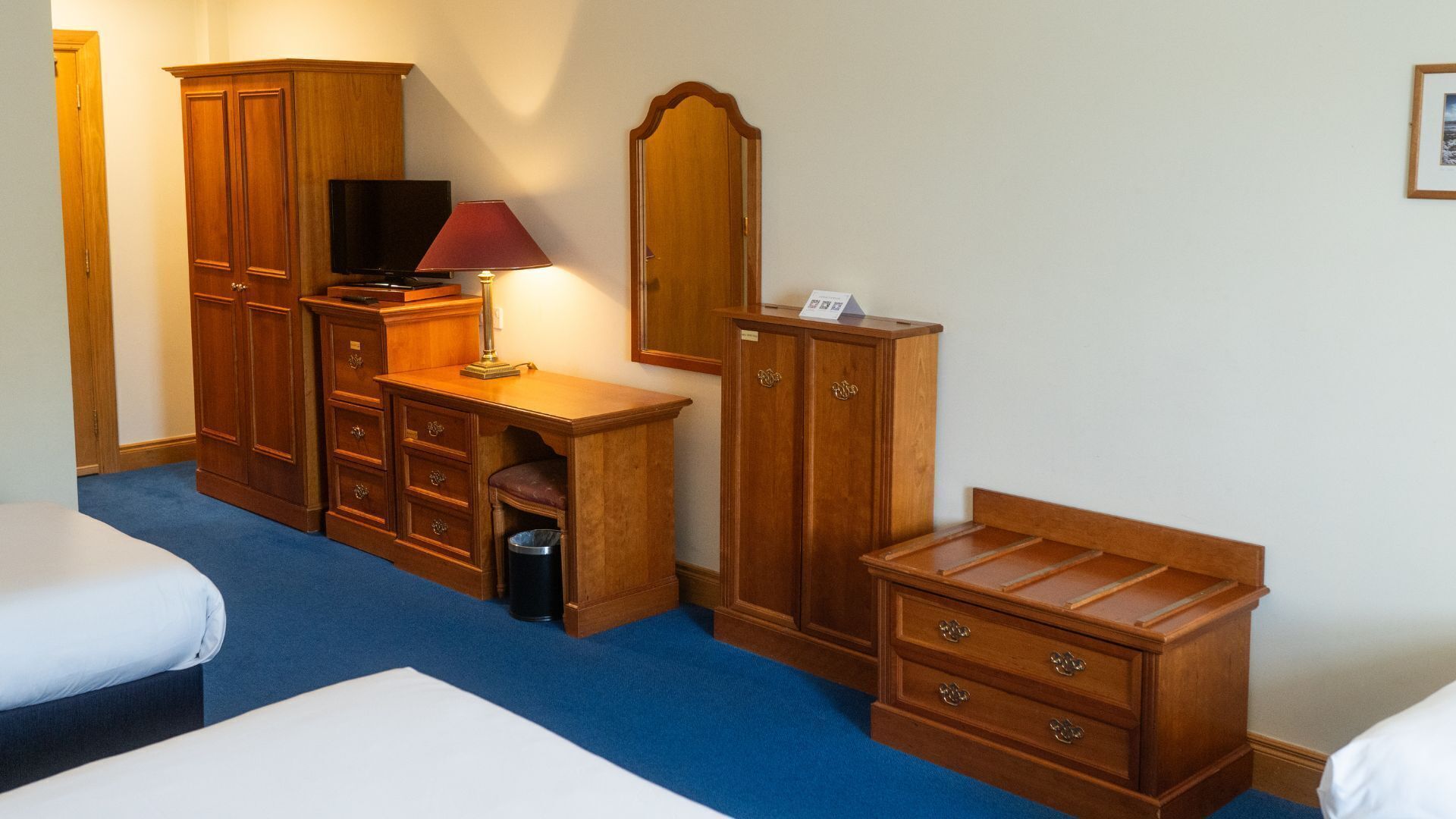 Una habitación de hotel con una cama, un escritorio con lámpara, un televisor y armarios de madera.