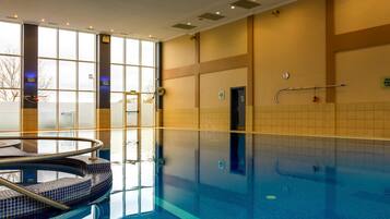 An indoor swimming pool with clear water, a diving board, and a lifeguard chair.