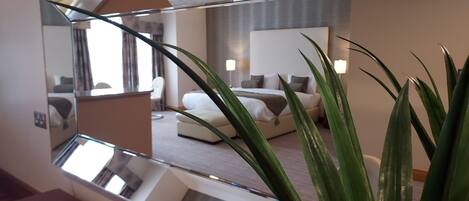 A modern hotel room with a large mirror reflecting the interior, a bed, a sofa, and a potted plant.