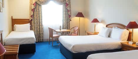A hotel room with two single beds, a small table with a chair, and two bedside lamps.