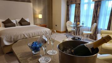 Et hotelværelse med en seng, et spisebord med vinglas og en champagneflaske, samt et lille bord med en skål chokolade.