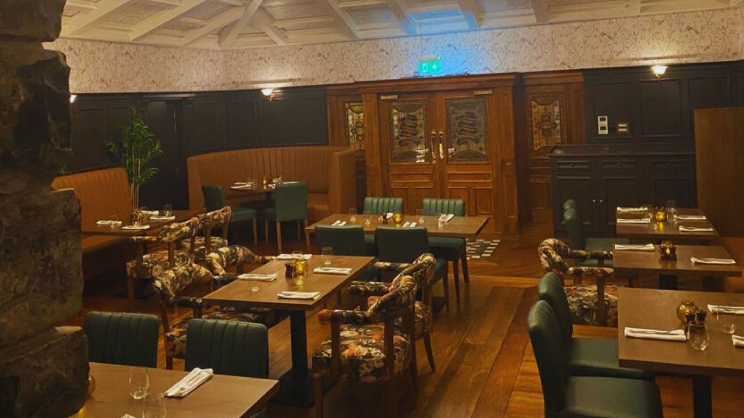 Un restaurant avec des tables et des chaises en bois, un mur en pierre et un plafond doté d’une lucarne.