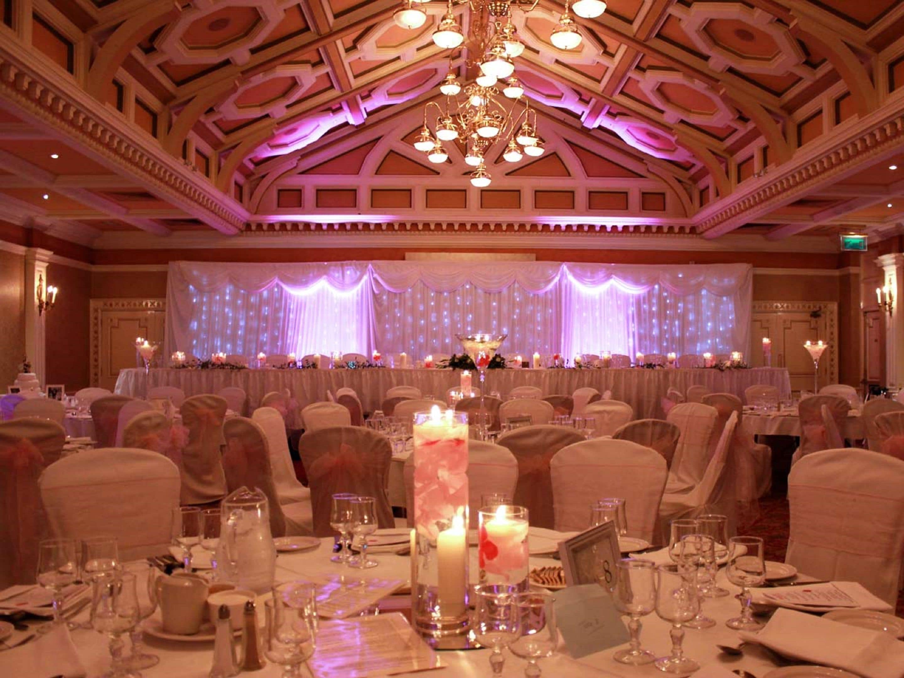 A banquet hall with tables set for a formal event, featuring a stage with draped curtains and a chandelier.