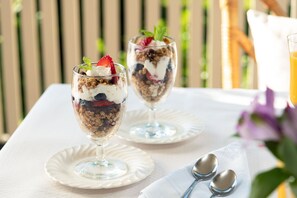 Dos vasos de postre sobre platos blancos, junto a un mantel blanco, acompañados de dos cucharas y una servilleta.