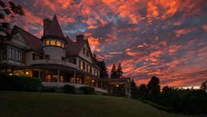 A large, multi-story house with a wrap-around porch and multiple chimneys, set against a dramatic sunset sky. - Idlwilde Inn (Watkins Glen)