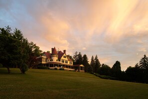 A large, multi-story house with a wrap-around porch and a turret, surrounded by a well-maintained lawn and trees. - Idlwilde Inn (Watkins Glen)