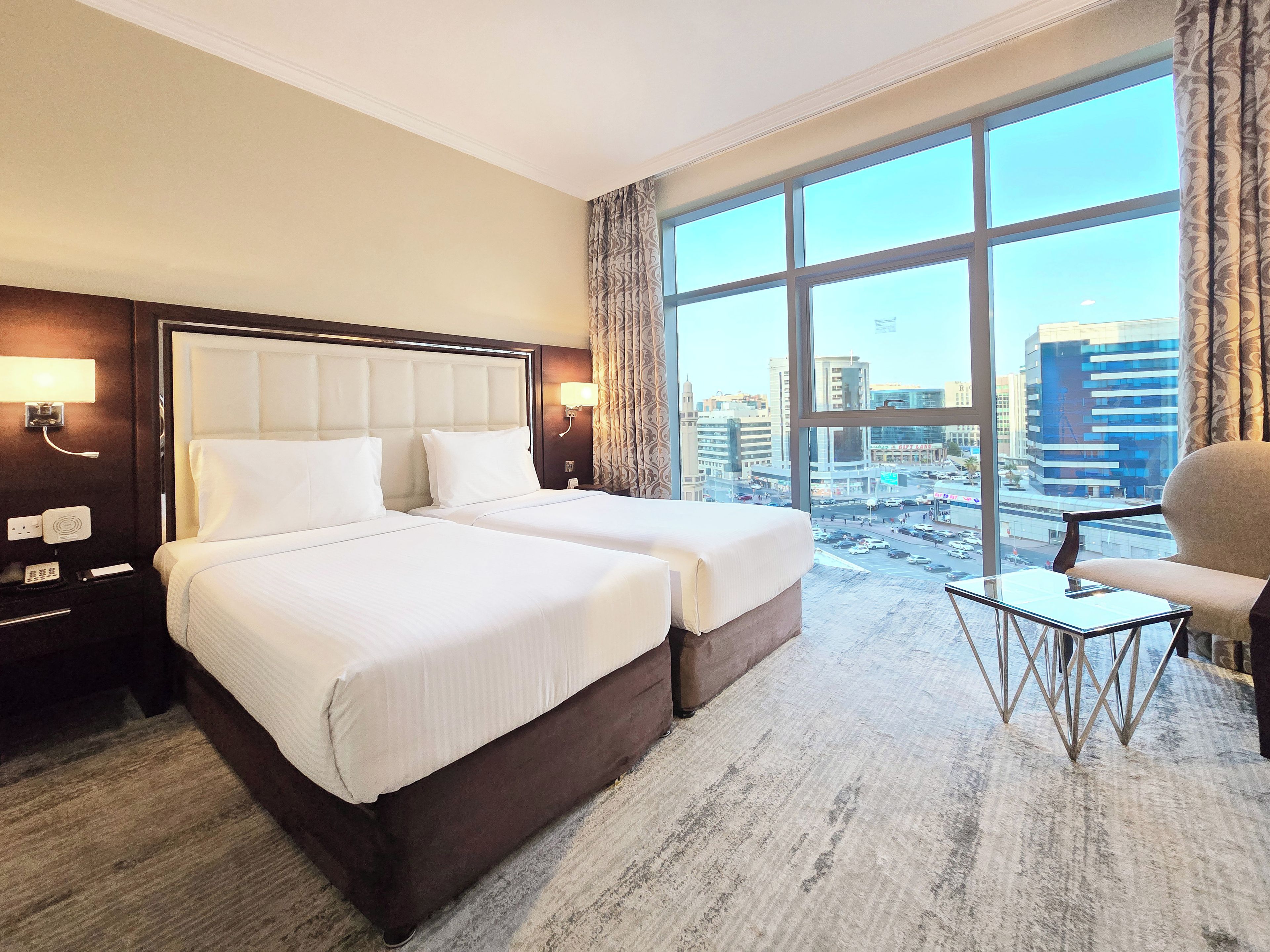 A hotel room with two beds, a view of the city, and a small table.