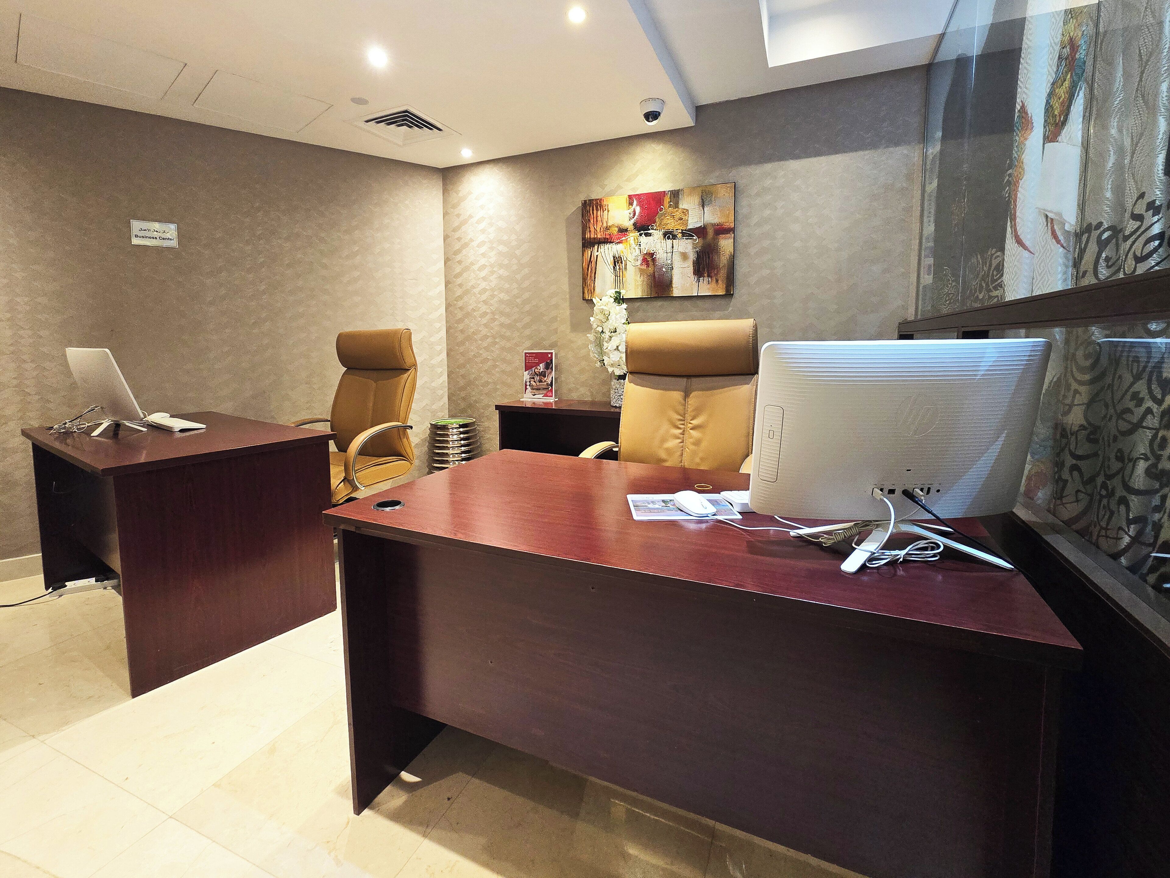 A conference room with a wooden desk, two leather chairs, a computer, and a glass partition.