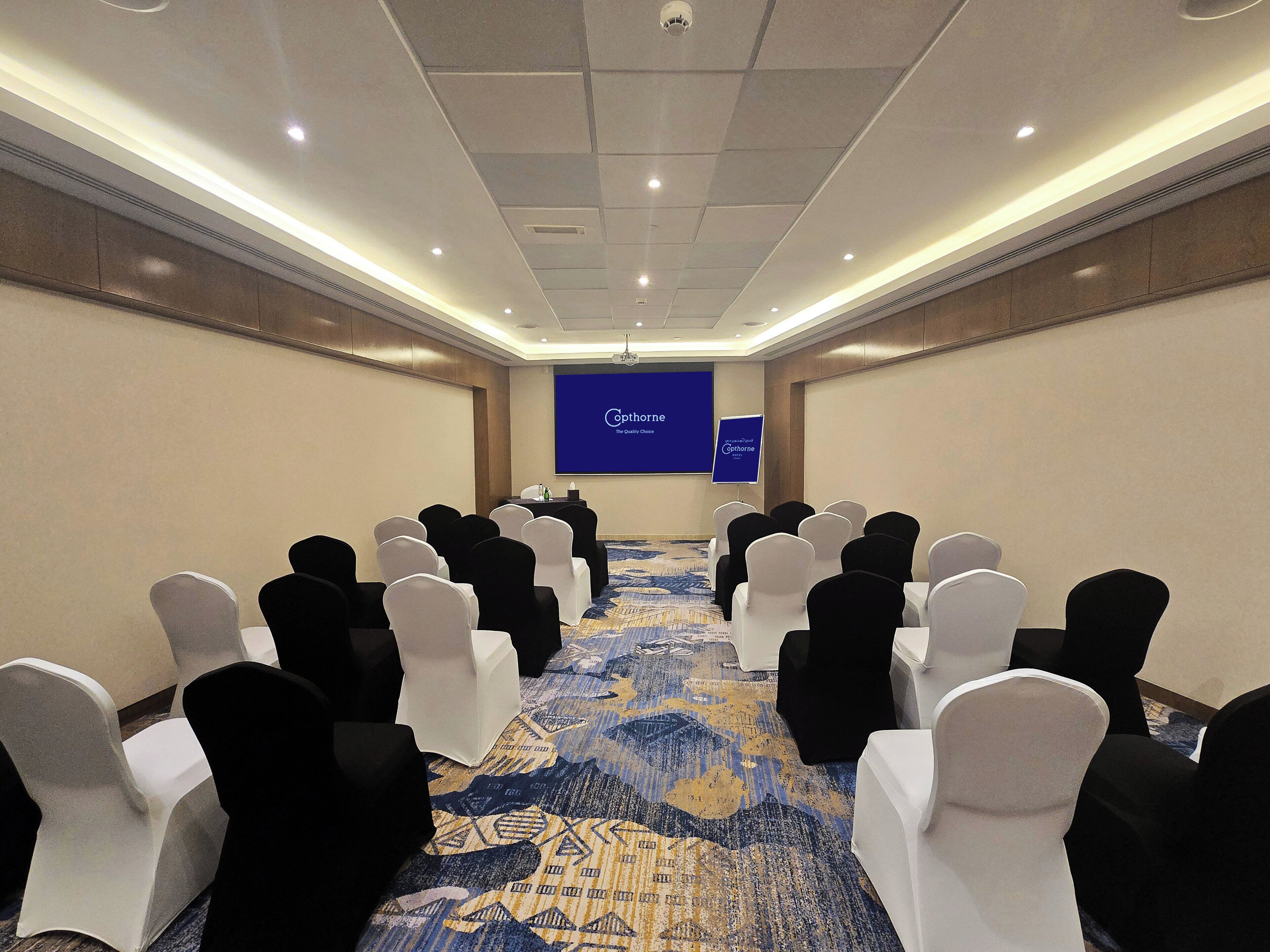 A conference room with rows of chairs, a projector screen, and a carpeted floor.
