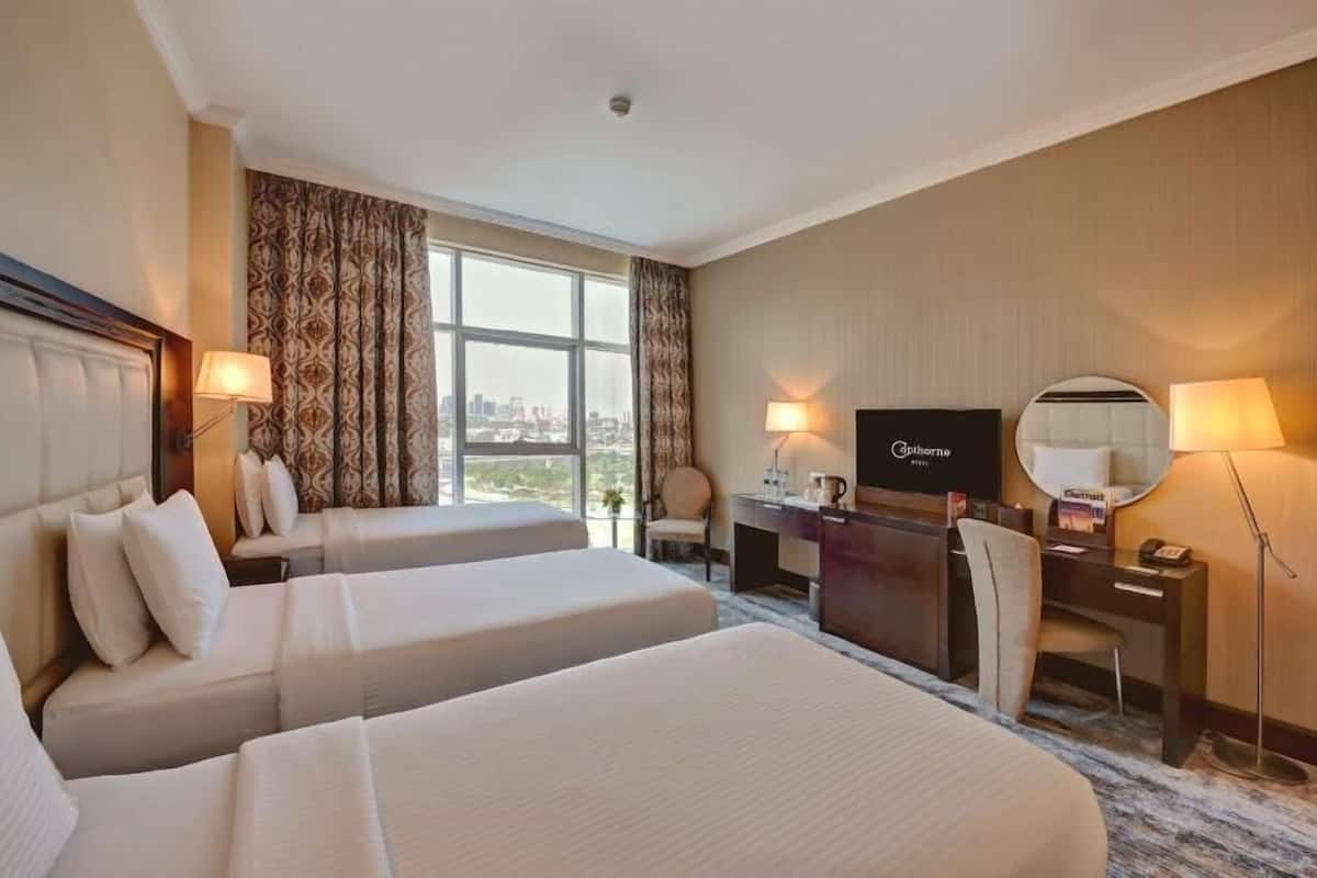 A hotel room with two beds, a desk, a chair, a TV, and a view of the city.