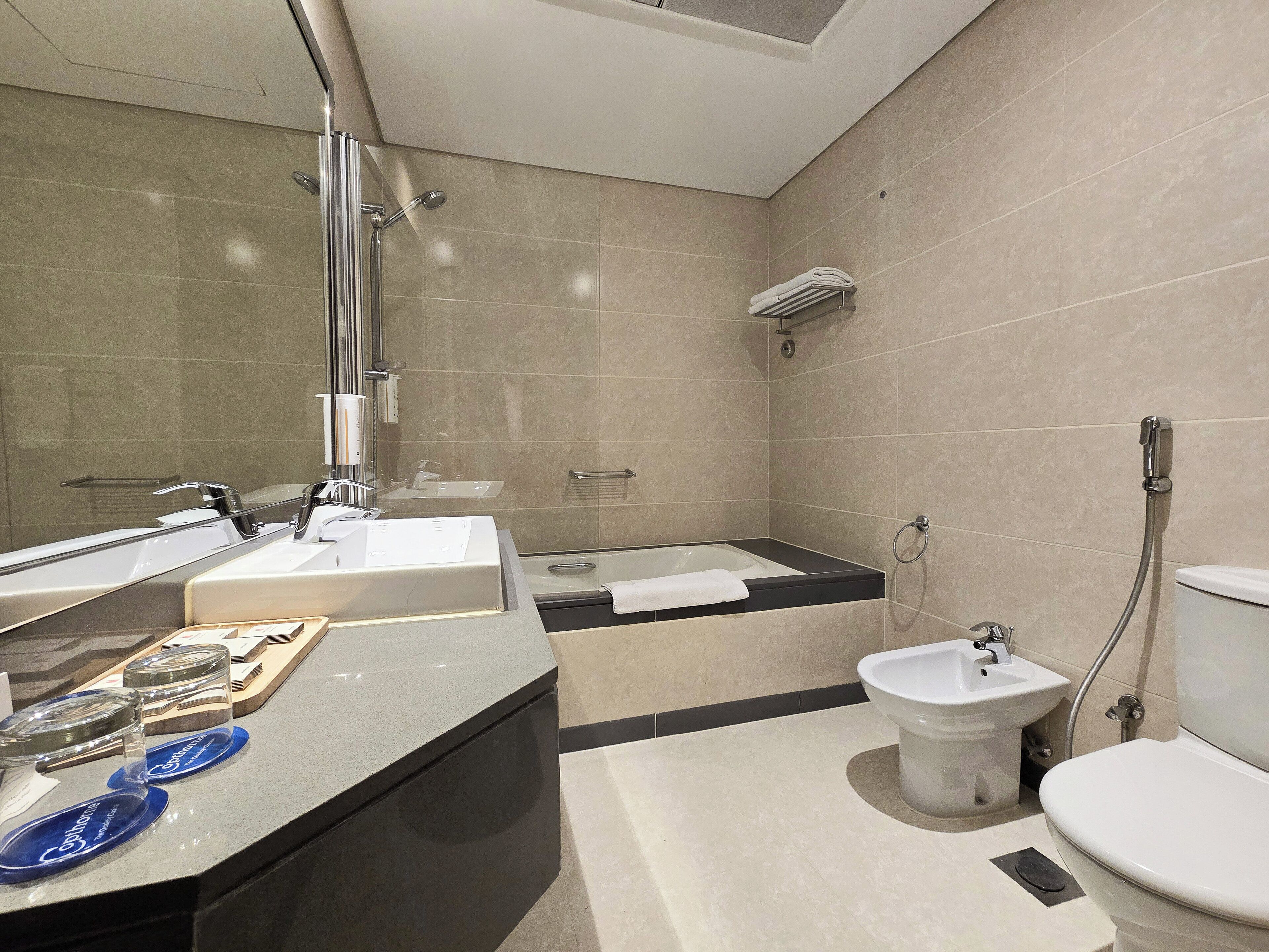 Een moderne badkamer met een grote spiegel, een badkuip, een toilet en een wastafel.