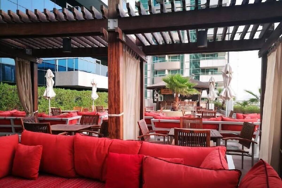 Un espace extérieur abrité, aménagé avec des coussins rouges, des tables en bois et des parasols.