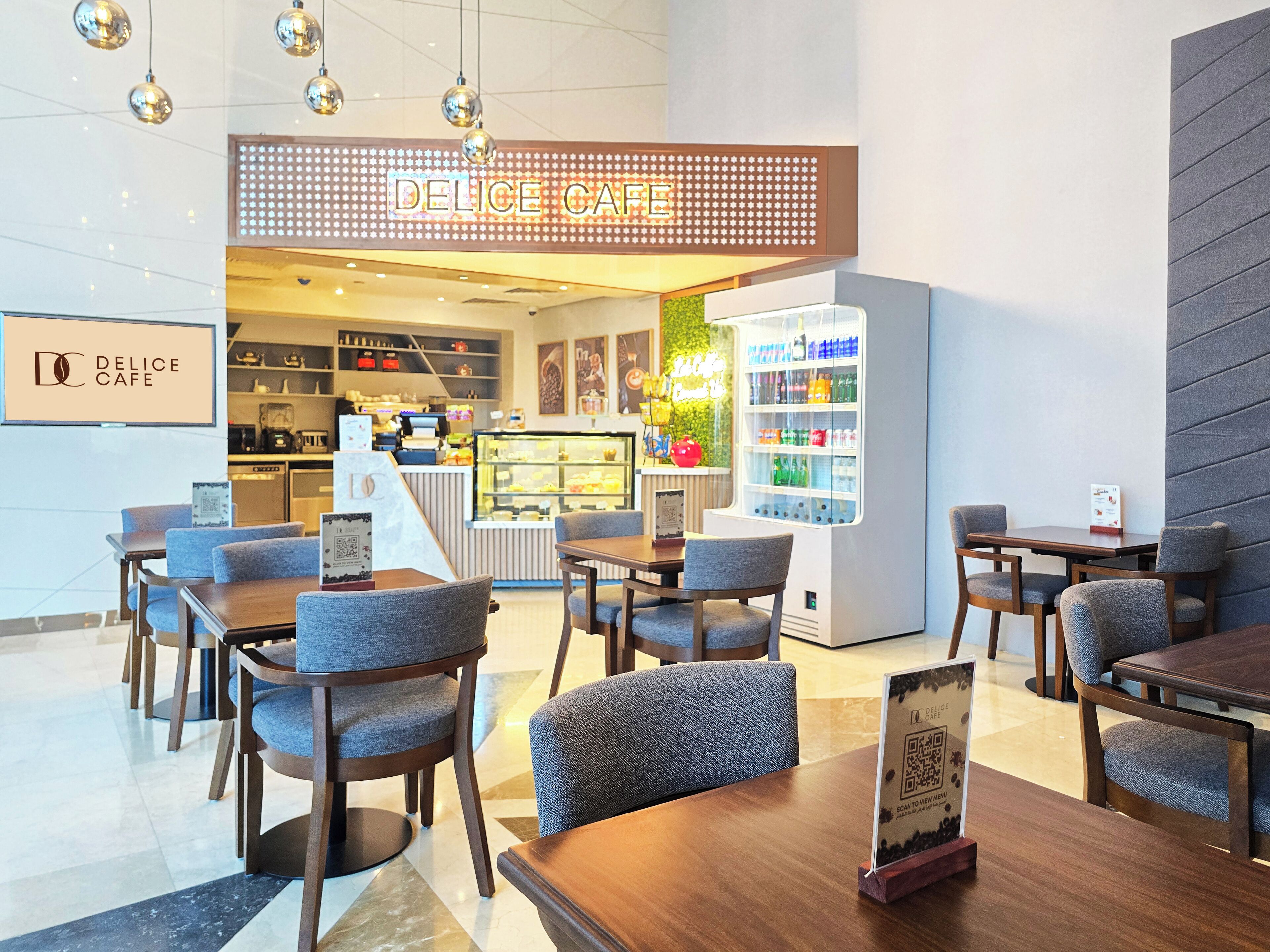 Ein modernes Café-Interieur mit Holztischen und -stühlen, einer Vitrine mit Gebäck und einem Neon-Schild mit der Aufschrift 'DELICE CAFE'.