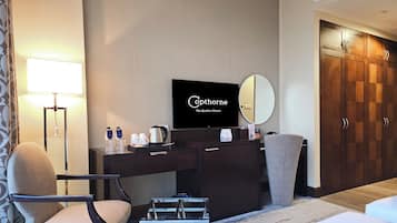 Une chambre d’hôtel comprenant un lit, un bureau avec un téléviseur à écran plat, une chaise, une lampe de bureau, une machine à café et une armoire.