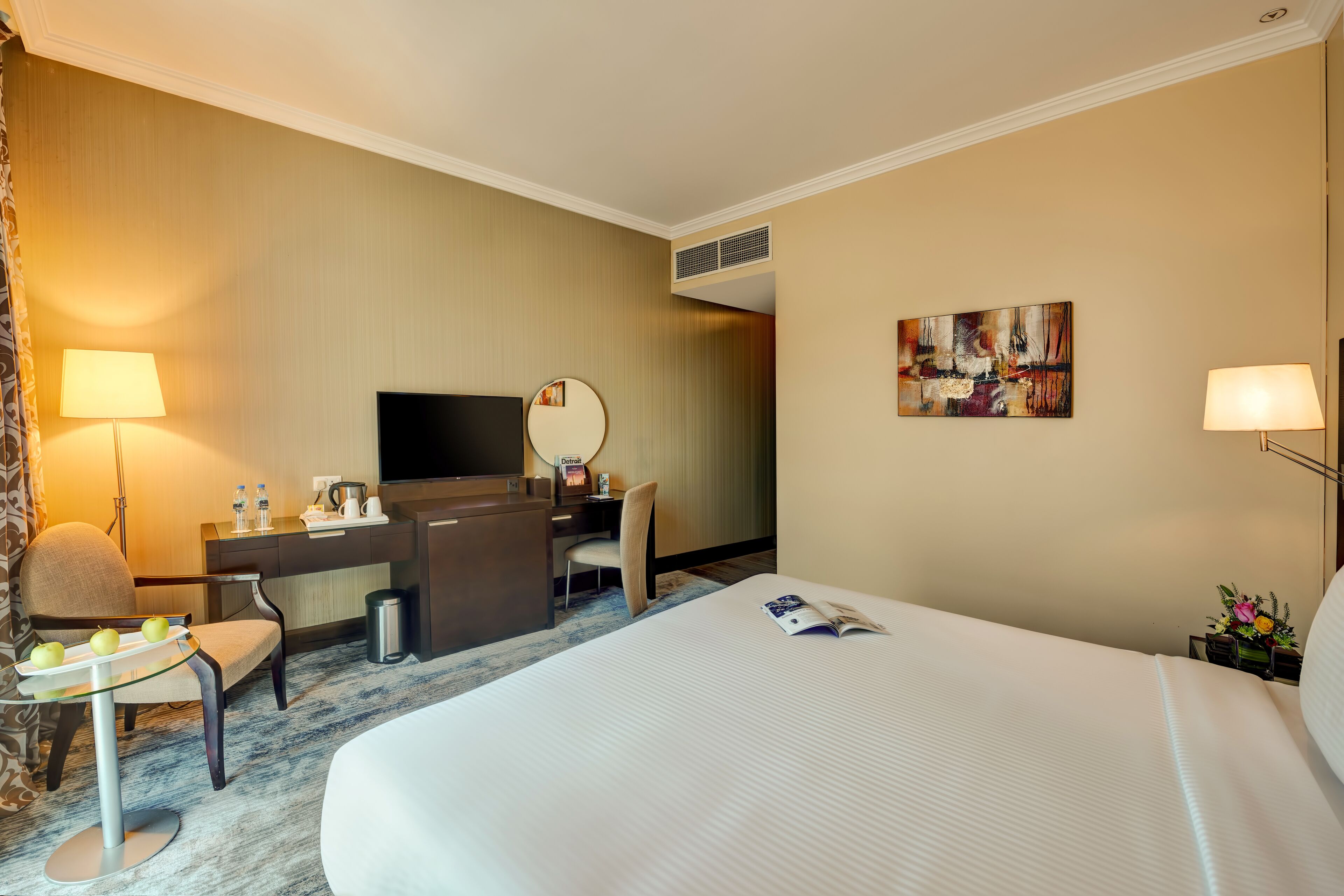 Quarto de hotel com cama, escrivaninha, cadeira, televisão e obras de arte.