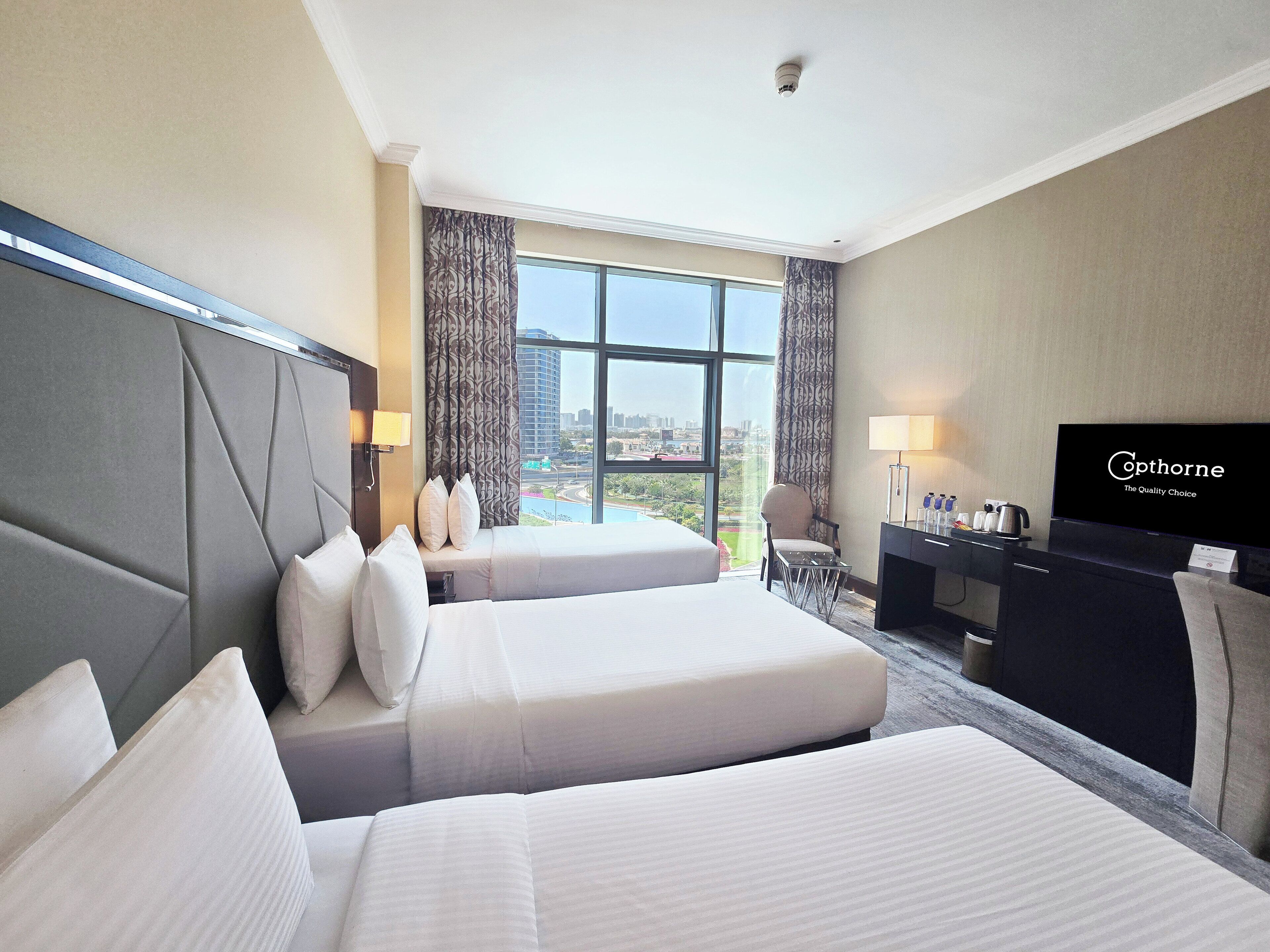 Ein Hotelzimmer mit zwei Betten, einem Schreibtisch, einem Fernseher und Blick auf die Stadt.