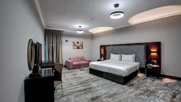 A modern hotel room with a large bed, a desk, a pink sofa, and a small table.