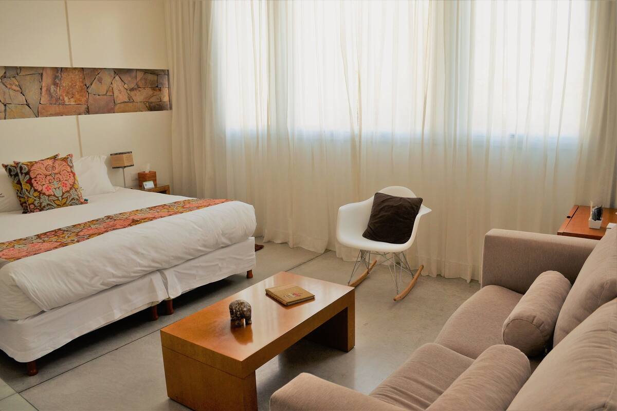Habitació d'hotel amb llit, sofà, taula de cafè, cadira i una paret decorativa de pedra.