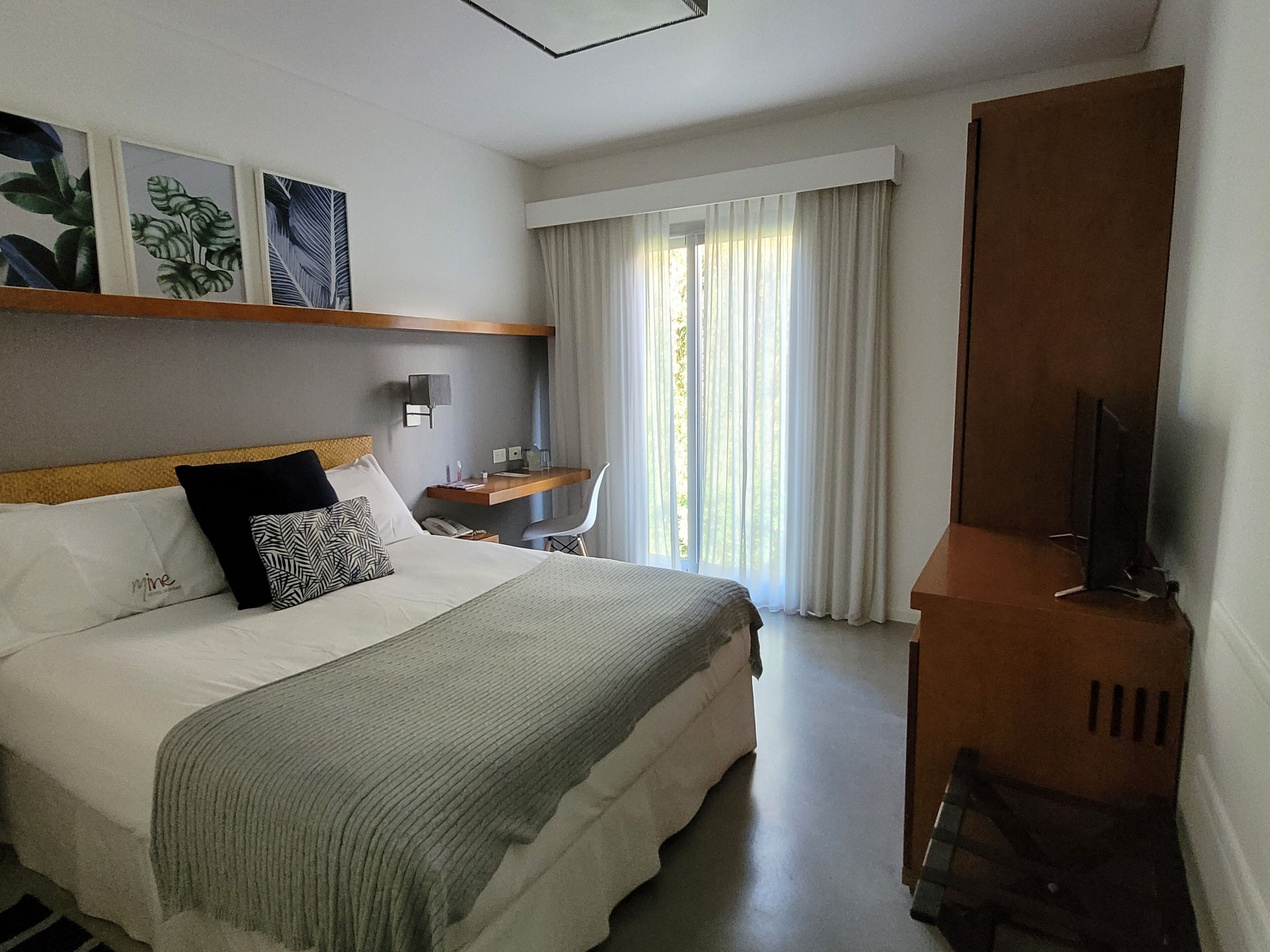 A hotel room with a bed, a desk, a chair, a television, and a window with curtains.