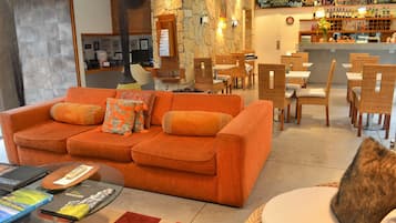 A hotel lobby with a large orange sofa, wicker chairs, a bar area with a wine selection, and a stone accent wall.