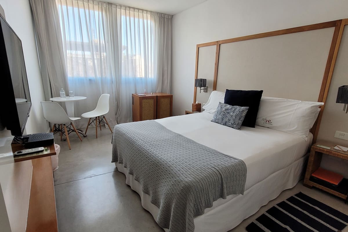 Una habitació d'hotel amb un llit gran, un escriptori amb un ordinador, una cadira, una taula petita i una finestra amb cortines.