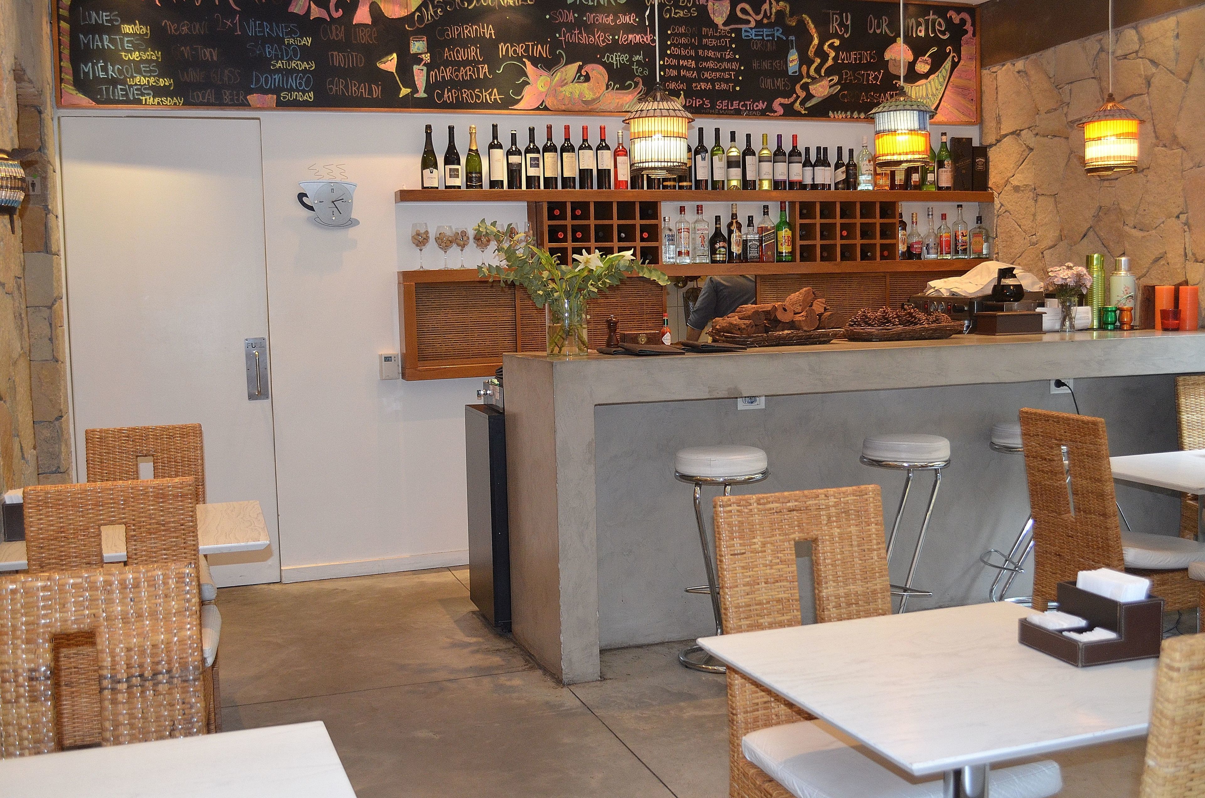 A bar area with a variety of bottles, a chalkboard menu, and wicker furniture.
