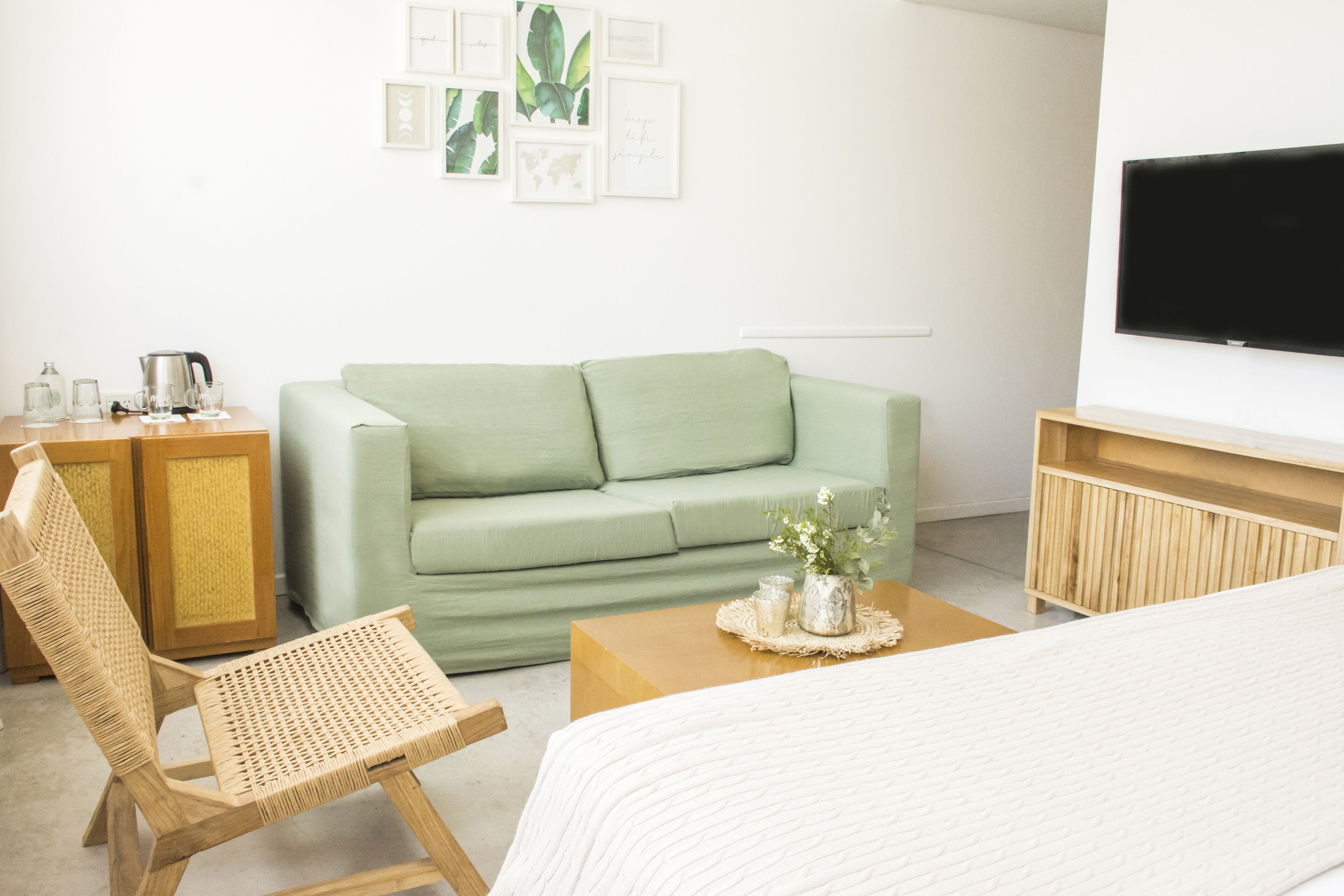 Una habitación con un sofá verde, una silla de madera, una mesa de centro con un jarrón, un televisor y un mueble de madera.