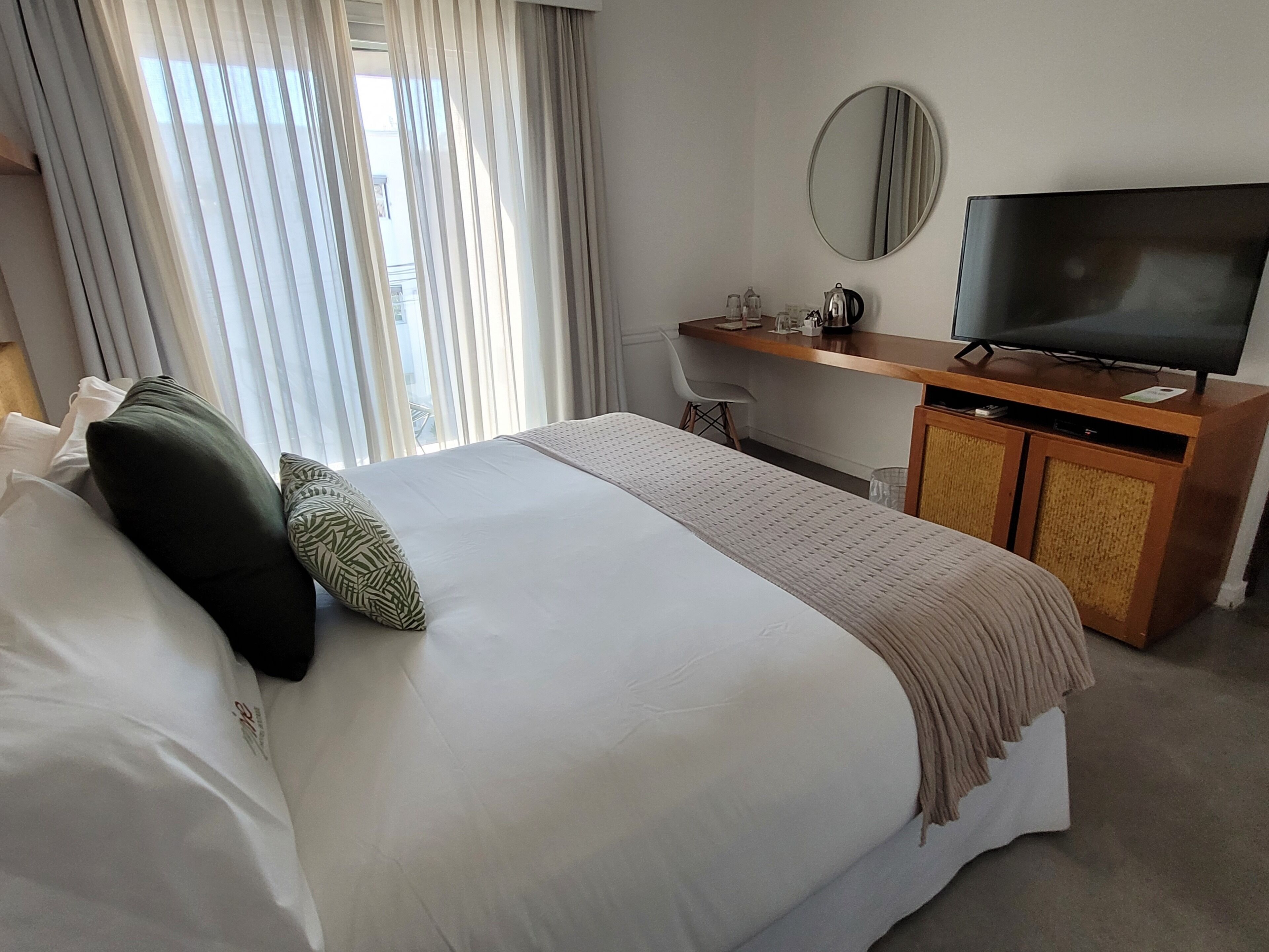 A hotel room with a large bed, a TV on a wooden cabinet, and a window with curtains.