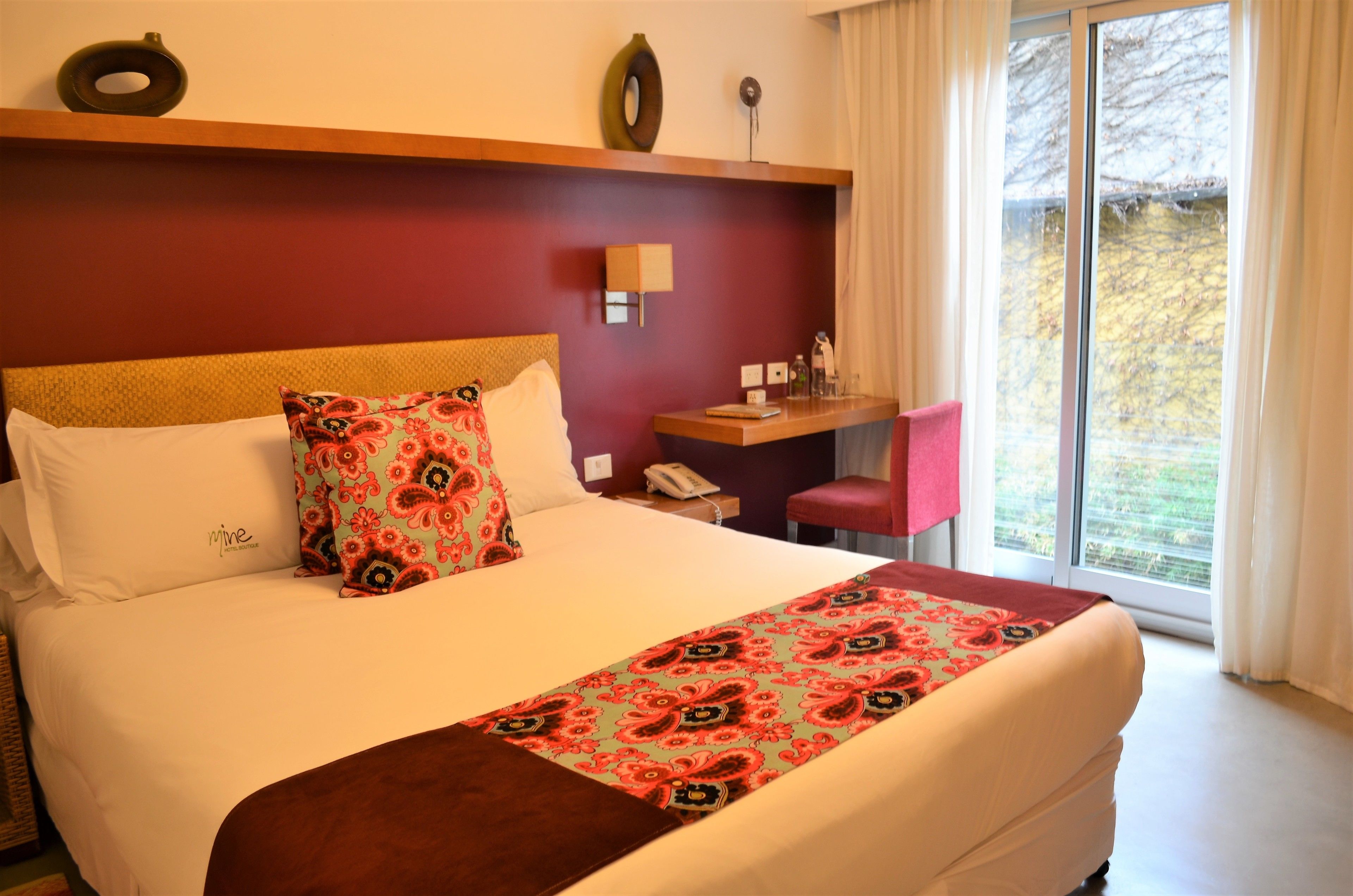 A hotel room with a large bed, a desk, and a window with curtains.