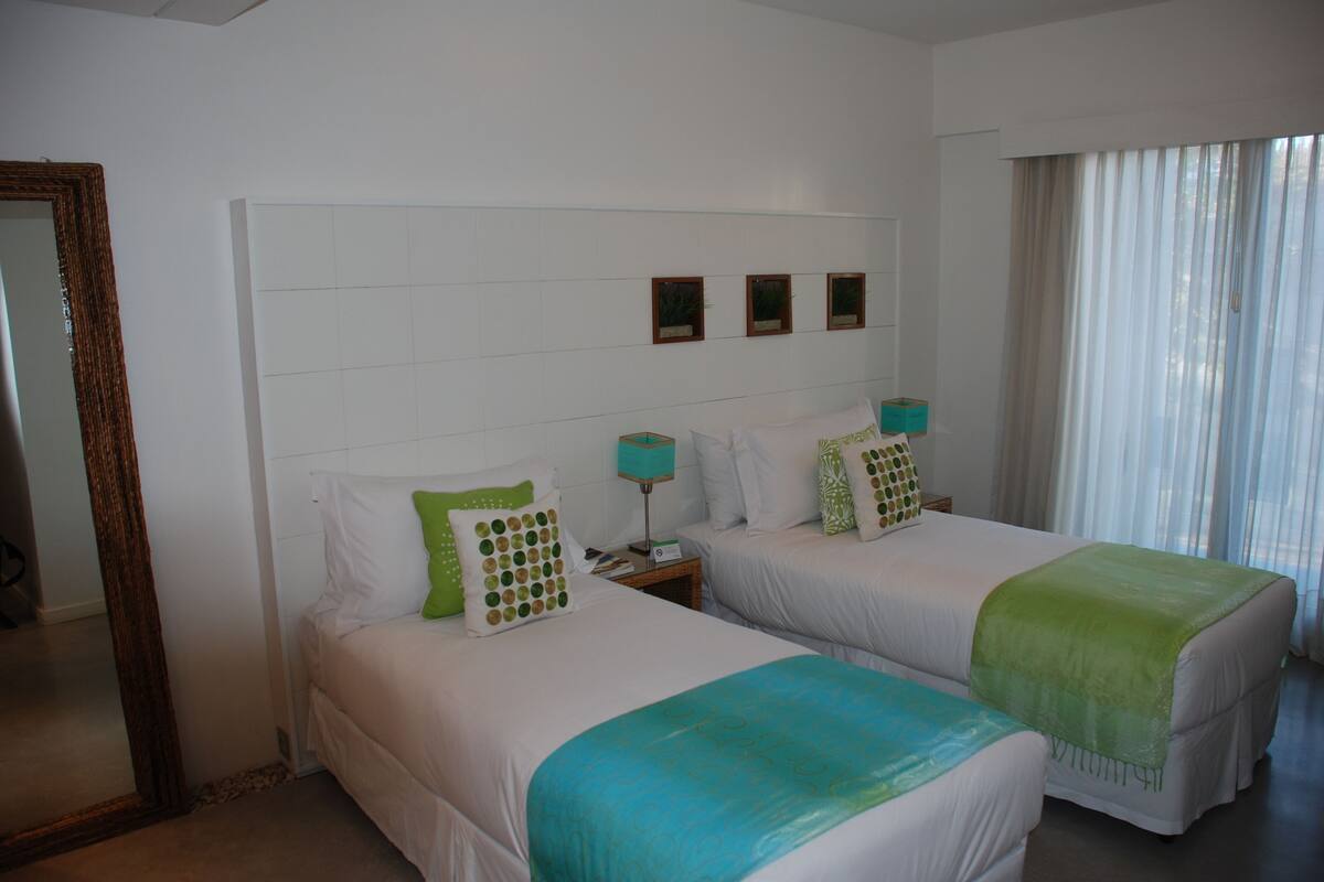 Habitació d'hotel amb dos llits, un mirall gran i una finestra amb cortines translúcides.