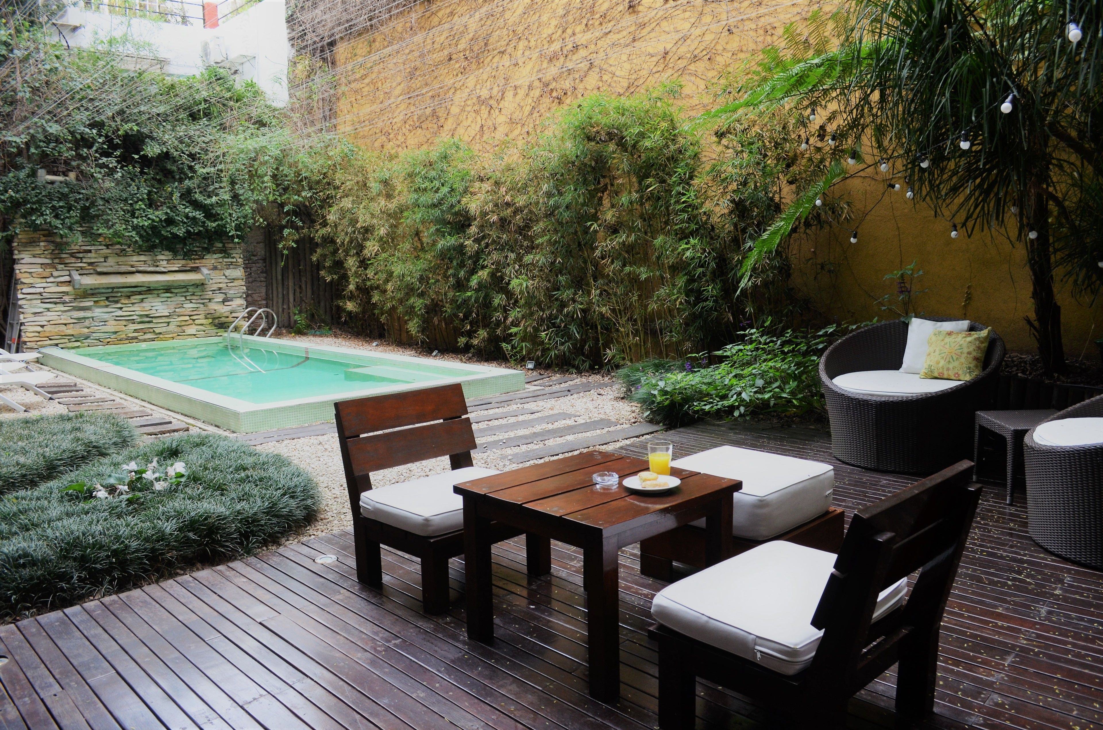 Eine Holzterrasse mit Pool, Gartenmöbeln und üppiger Bepflanzung.