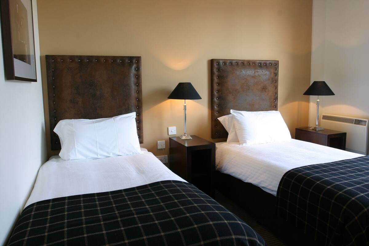 Ein Hotelzimmer mit zwei Betten, jeweils mit Kopfteil, Nachttischen, Lampen und einer weißen Bettdecke.