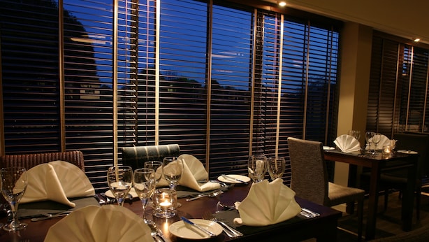 A dining table set for a meal with chairs, a candle, and wine glasses.